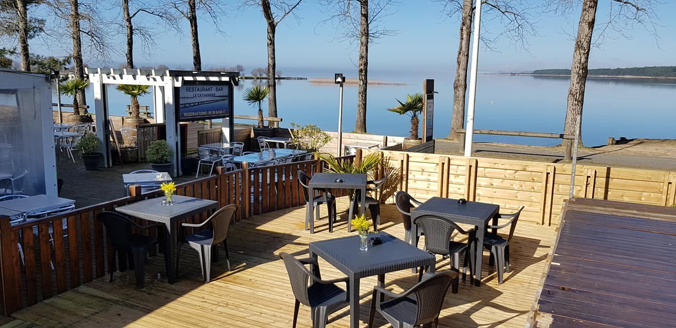 Terraza de madera del Catamaran frente al lago de Sanguinet, con mesas, parasoles y palmeras